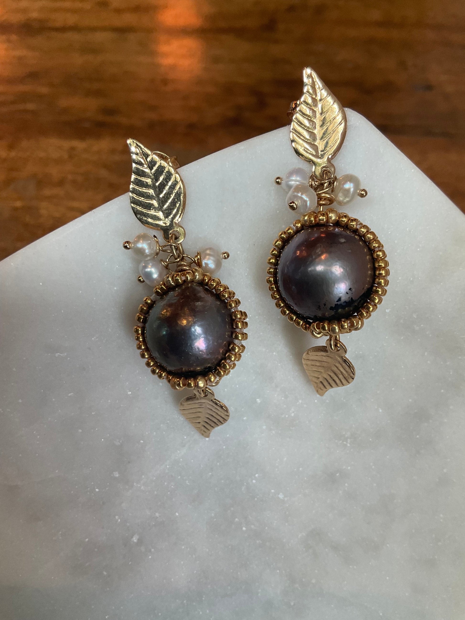 Black South Sea “Tahitian” pearls encased in free form net beading on gold-filled leaf posts with tiny fresh water pearls dangling from the leaves and a gold-filled leaf dangling from the black pearl.