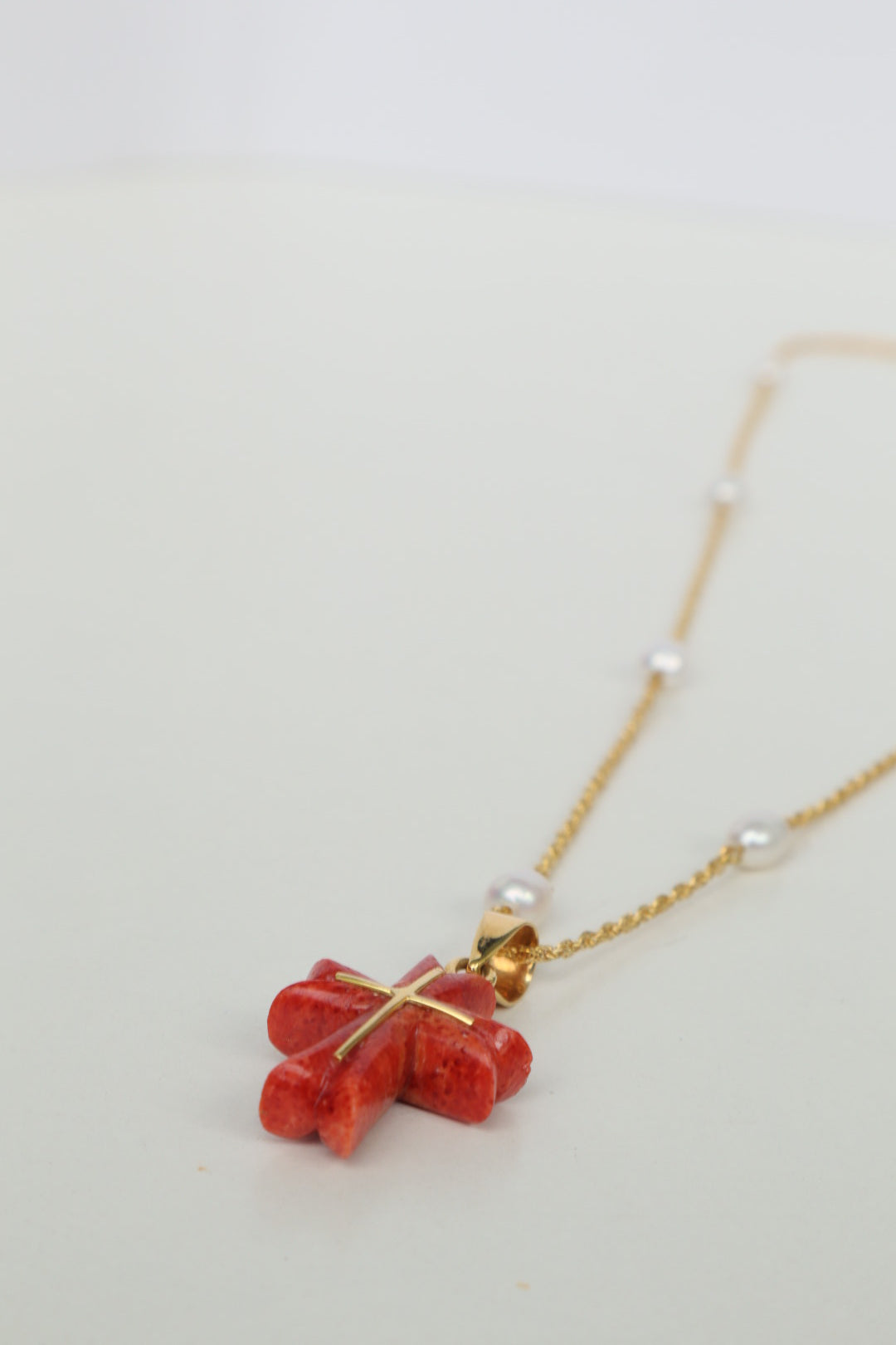 Luminous freshwater pearls add a touch of elegance, while the stunning Japanese coral cross pendant, in a fiery shade of red, takes center stage. The coral is intricately detailed with an inlaid 18K gold cross, a symbol of hope and devotion. All elements are strung on a delicate 18K gold chain.