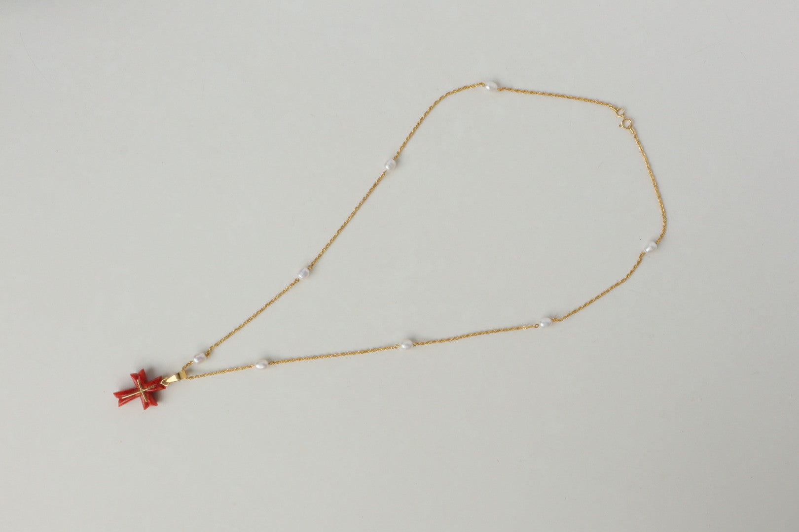 Luminous freshwater pearls add a touch of elegance, while the stunning Japanese coral cross pendant, in a fiery shade of red, takes center stage. The coral is intricately detailed with an inlaid 18K gold cross, a symbol of hope and devotion. All elements are strung on a delicate 18K gold chain.