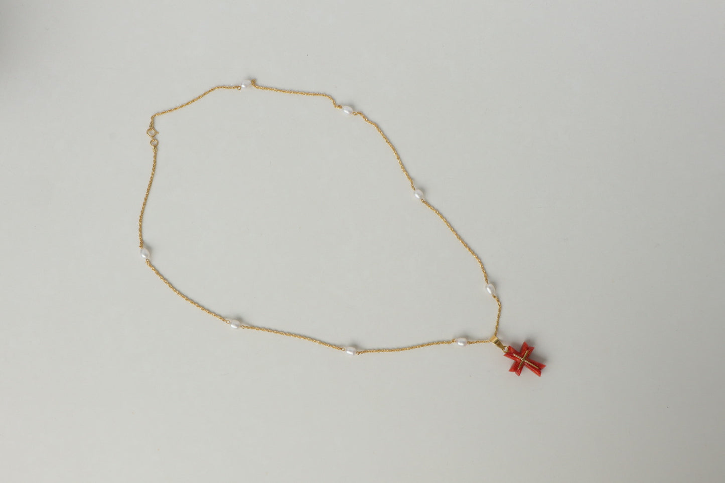 Luminous freshwater pearls add a touch of elegance, while the stunning Japanese coral cross pendant, in a fiery shade of red, takes center stage. The coral is intricately detailed with an inlaid 18K gold cross, a symbol of hope and devotion. All elements are strung on a delicate 18K gold chain.