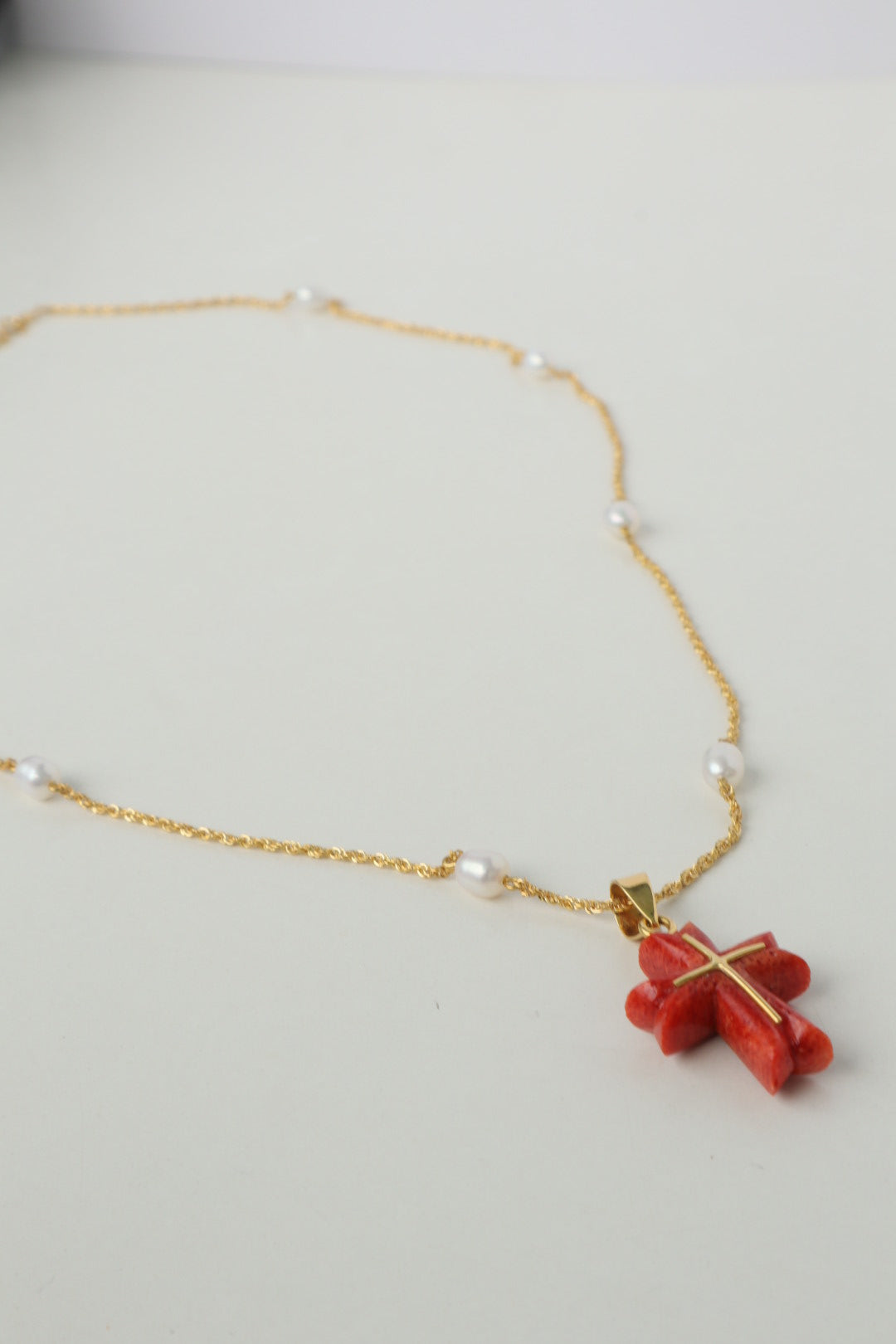 Luminous freshwater pearls add a touch of elegance, while the stunning Japanese coral cross pendant, in a fiery shade of red, takes center stage. The coral is intricately detailed with an inlaid 18K gold cross, a symbol of hope and devotion. All elements are strung on a delicate 18K gold chain.