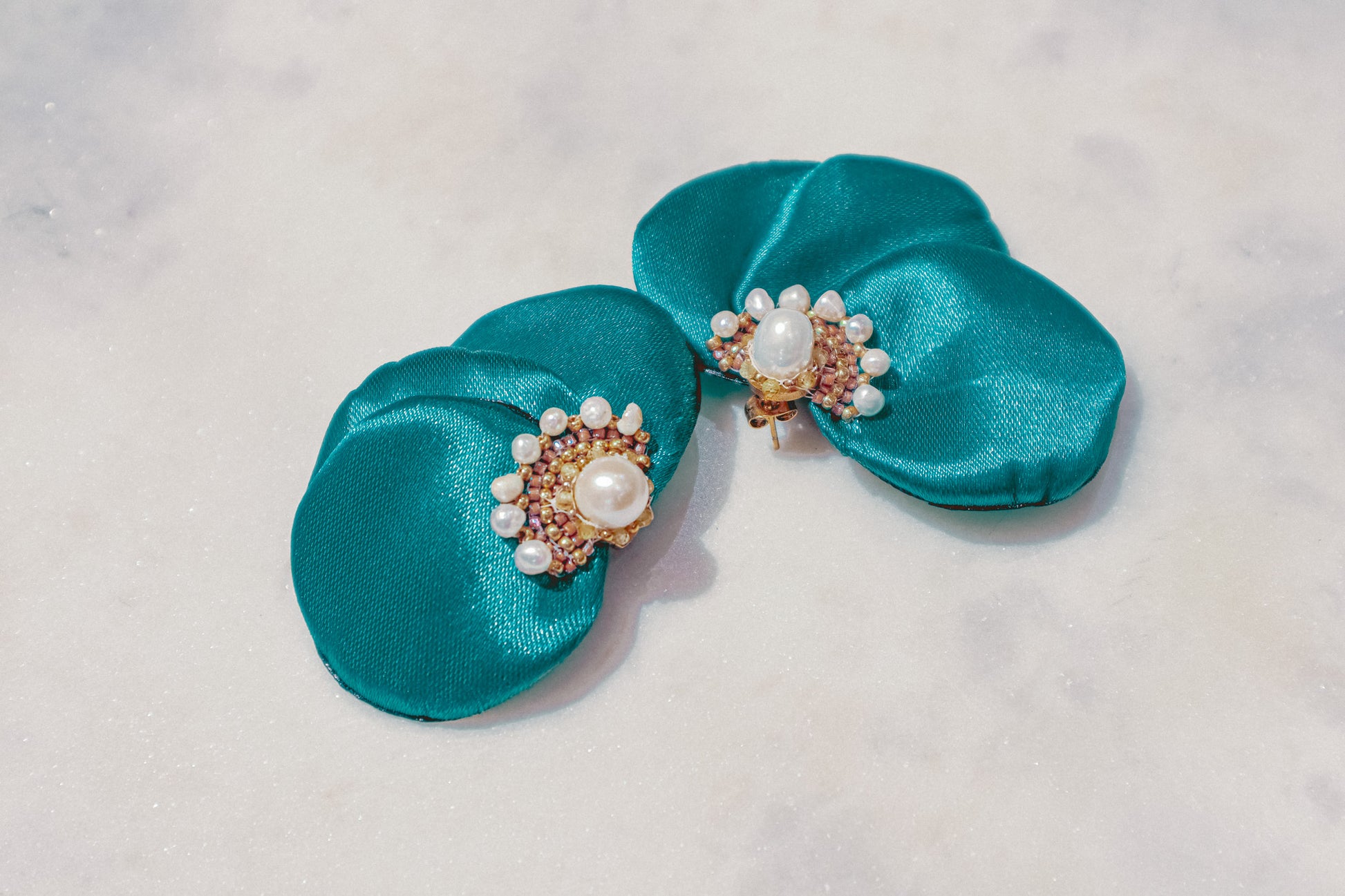 Celebrate the vibrant energy of summer with these captivating blue-green silk flower fan earrings. The meticulously embroidered design, featuring shimmering Miyuki beads, brings the flower to life. Delicate freshwater pearls and sparkling lemon sapphires add a touch of sophistication, making these earrings a perfect way to add a burst of color to any outfit.