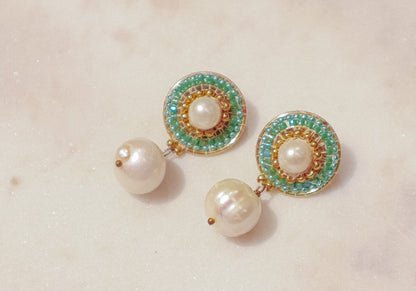 These earrings showcase a captivating interplay of classic and modern design. Luminous pearl drops exude timeless elegance, while shimmering green Miyuki beads, meticulously woven around the posts, add a touch of modern flair. Secured on gleaming 18k gold-filled posts, these earrings are perfect for everyday wear or a touch of elegance for a special occasion