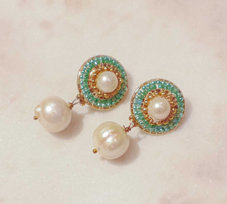 These earrings showcase a captivating interplay of classic and modern design. Luminous pearl drops exude timeless elegance, while shimmering green Miyuki beads, meticulously woven around the posts, add a touch of modern flair. Secured on gleaming 18k gold-filled posts, these earrings are perfect for everyday wear or a touch of elegance for a special occasion