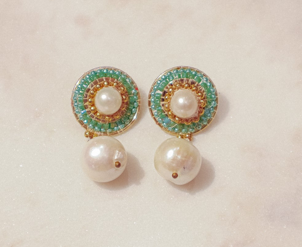 These earrings showcase a captivating interplay of classic and modern design. Luminous pearl drops exude timeless elegance, while shimmering green Miyuki beads, meticulously woven around the posts, add a touch of modern flair. Secured on gleaming 18k gold-filled posts, these earrings are perfect for everyday wear or a touch of elegance for a special occasion