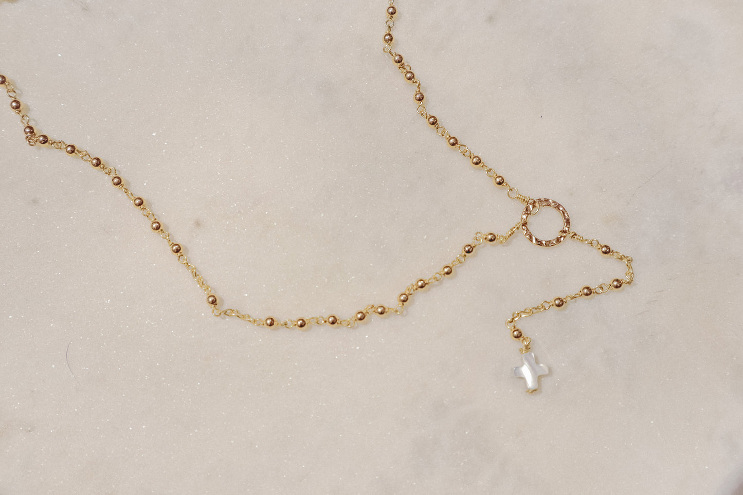 Delicate gold-filled balls adorn a sleek chain, leading to a luminous mother-of-pearl cross pendant.