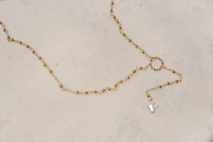 Delicate gold-filled balls adorn a sleek chain, leading to a luminous mother-of-pearl cross pendant.