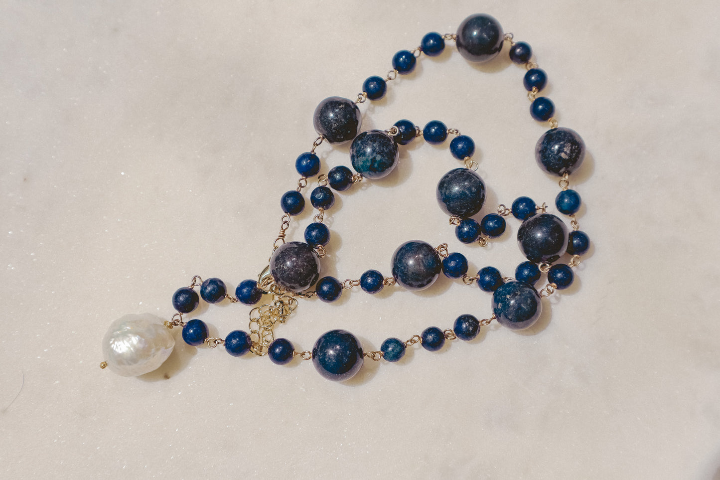 Rich lapis lazuli beads, a touch of the sea and sky, dance on a gleaming gold-filled wire chain. A luminous baroque pearl takes center stage, creating this statement piece necklace of simple beauty.