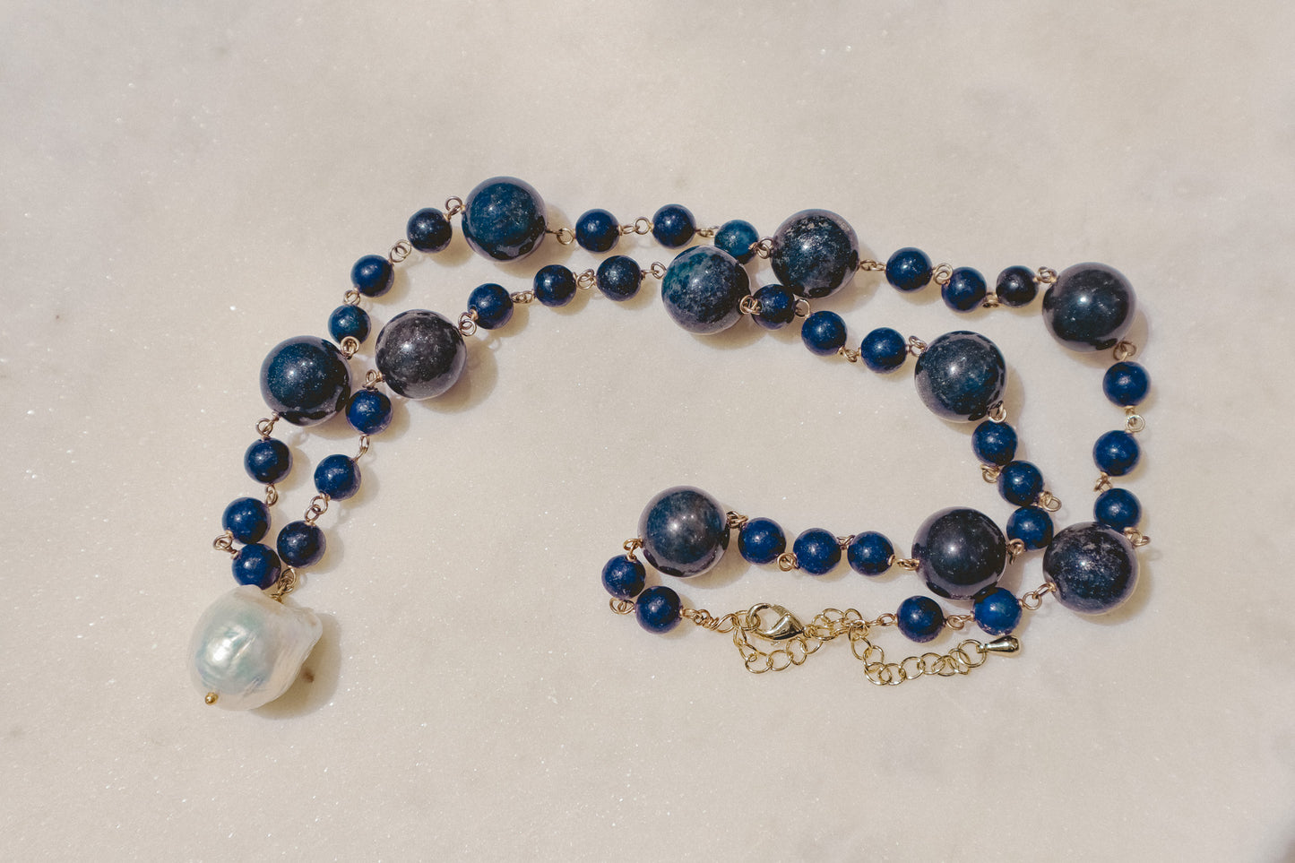 Rich lapis lazuli beads, a touch of the sea and sky, dance on a gleaming gold-filled wire chain. A luminous baroque pearl takes center stage, creating this statement piece necklace of simple beauty.