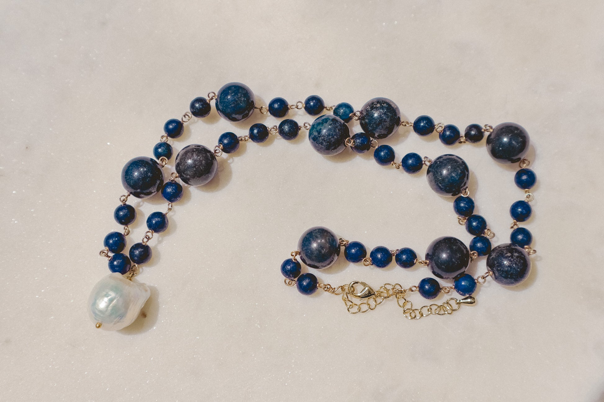 Rich lapis lazuli beads, a touch of the sea and sky, dance on a gleaming gold-filled wire chain. A luminous baroque pearl takes center stage, creating this statement piece necklace of simple beauty.