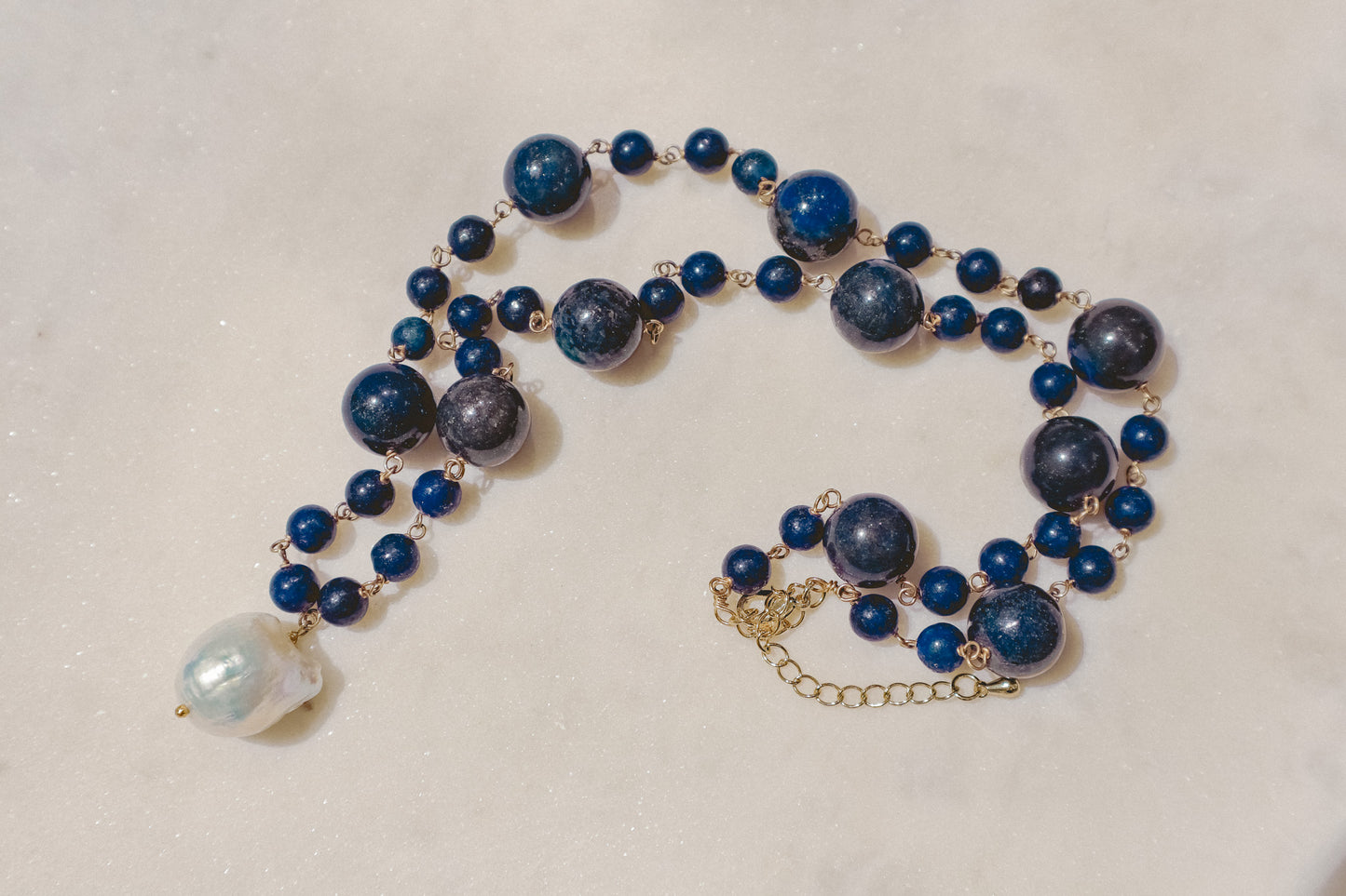 Rich lapis lazuli beads, a touch of the sea and sky, dance on a gleaming gold-filled wire chain. A luminous baroque pearl takes center stage, creating this statement piece necklace of simple beauty.