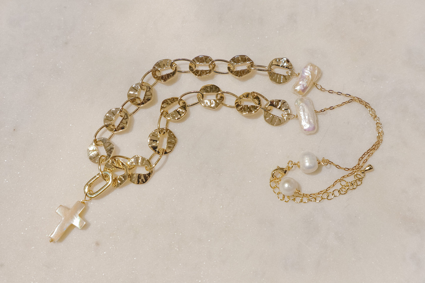 Freshwater pearls' timeless elegance rests on a shimmering gold-filled sand dollar chain, a symbol of protection. A delicate gold-filled enamel cross adds a touch of faith, creating a beautiful reminder of serenity and guidance.