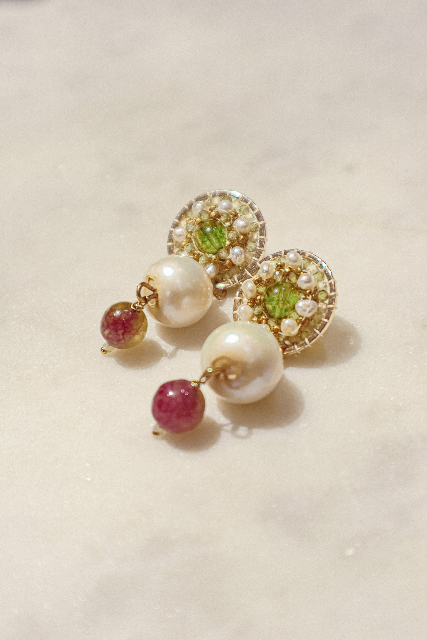 Celebrate a captivating interplay of gem and pearl with these 18k gold-filled earrings. Luminous peridot gemstones boast a refreshing lime green hue, symbolizing growth and prosperity. Tourmaline gemstones add a touch of vibrant color, mixing hues of deep pink to bright red. Organic baroque pearls whisper of elegance, while Keishi pearls add a touch of unique beauty. Secured on gleaming 18k gold-filled posts, these earrings are a captivating dance of texture, light, and symbolism.