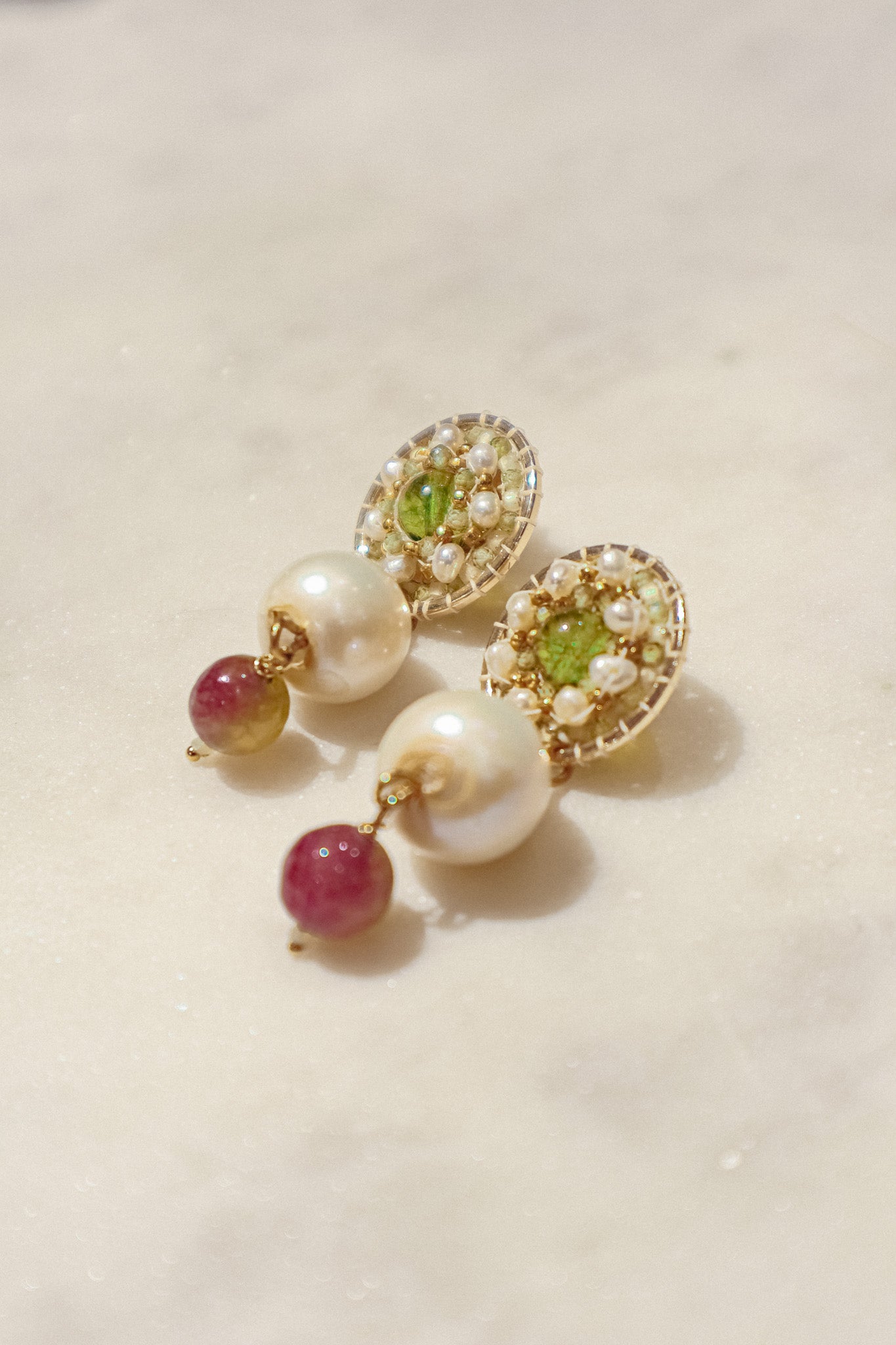 Celebrate a captivating interplay of gem and pearl with these 18k gold-filled earrings. Luminous peridot gemstones boast a refreshing lime green hue, symbolizing growth and prosperity. Tourmaline gemstones add a touch of vibrant color, mixing hues of deep pink to bright red. Organic baroque pearls whisper of elegance, while Keishi pearls add a touch of unique beauty. Secured on gleaming 18k gold-filled posts, these earrings are a captivating dance of texture, light, and symbolism.